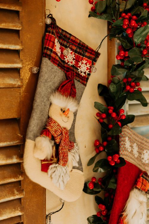 Free Cozy Christmas stocking with snowman and holiday decorations hanging on a rustic wall. Stock Photo