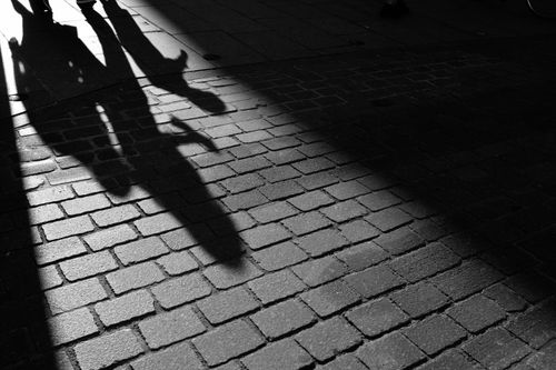 Free Silhouetted shadows of people walking on a cobblestone street in black and white. Stock Photo