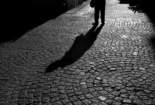Free Shadowy silhouette of a person walking along a patterned cobblestone street in black and white. Stock Photo
