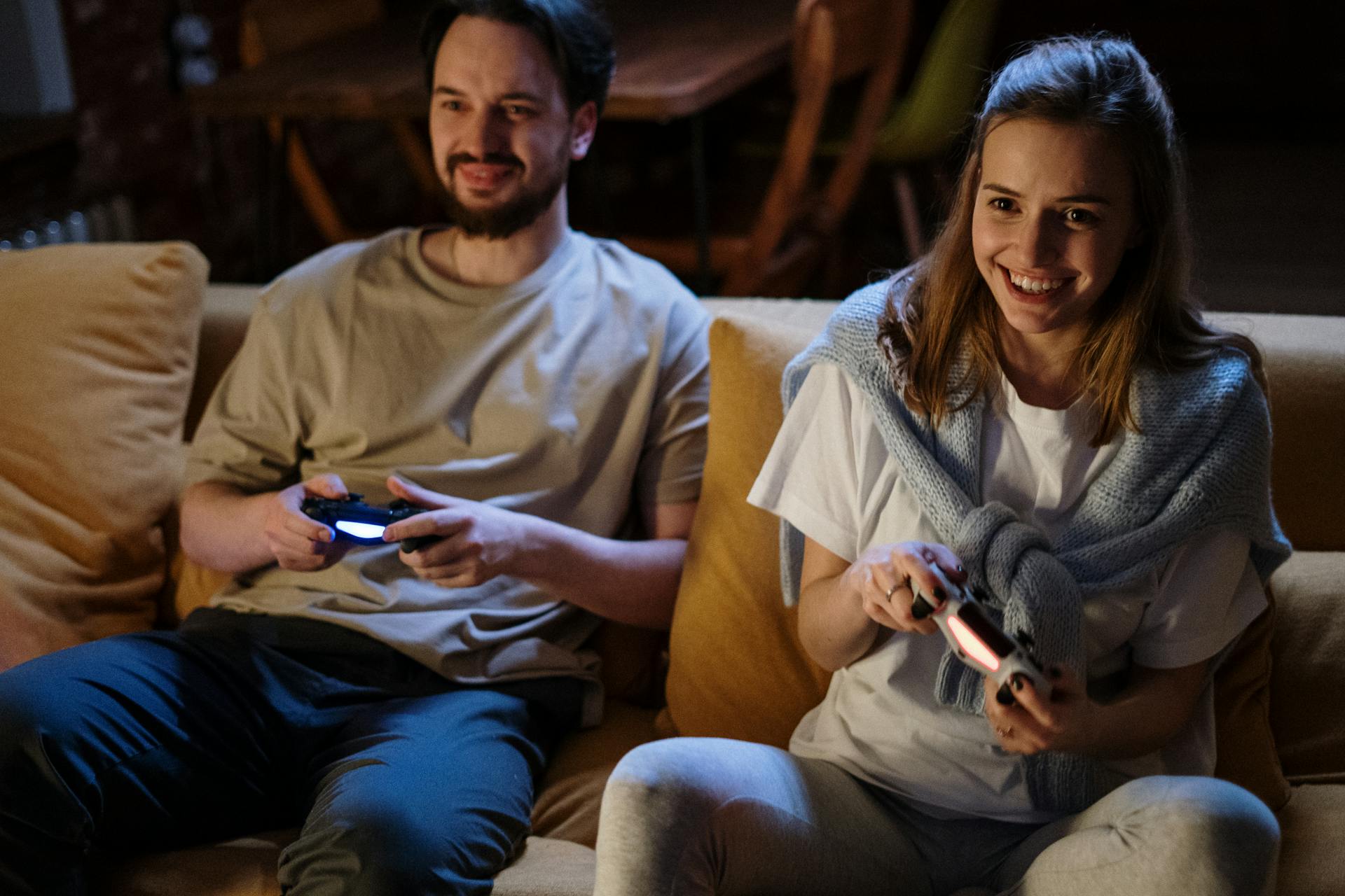 Smiling couple playing video games on couch at night, sharing joyful moments.