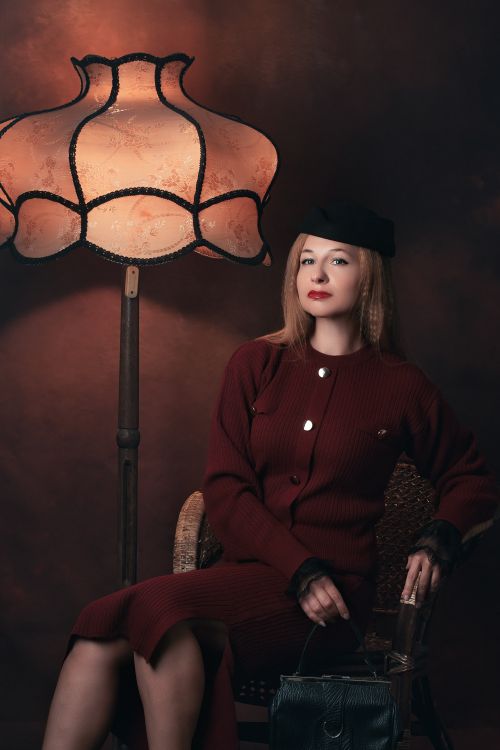Free Elegant woman in vintage attire sitting by a lamp, exuding classic charm. Stock Photo