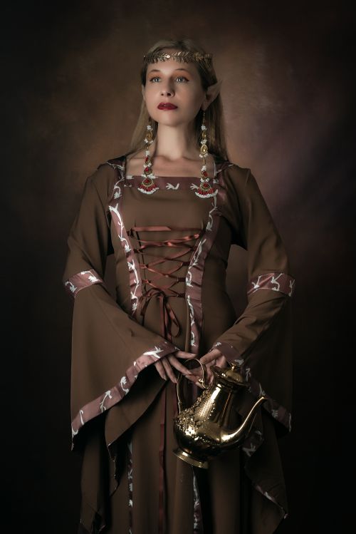 Free Elegant woman dressed as a fantasy elf holding a golden teapot in a medieval-style portrait. Stock Photo