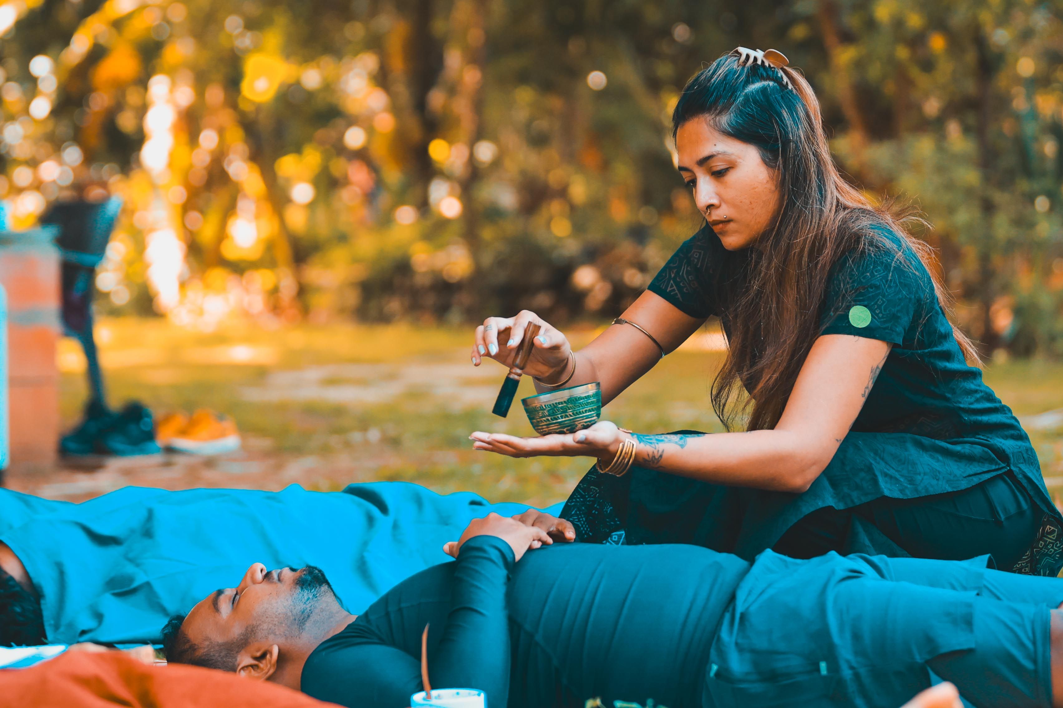 A woman applies essential oils to a resting person in a peaceful outdoor setting.