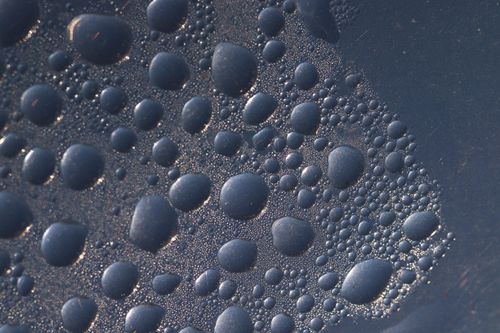 Free A macro shot of water droplets forming patterns on a dark surface. Stock Photo