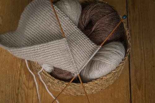 Free A close-up of a cozy knitting basket filled with beige and brown yarn and knitting needles on a wooden surface. Stock Photo