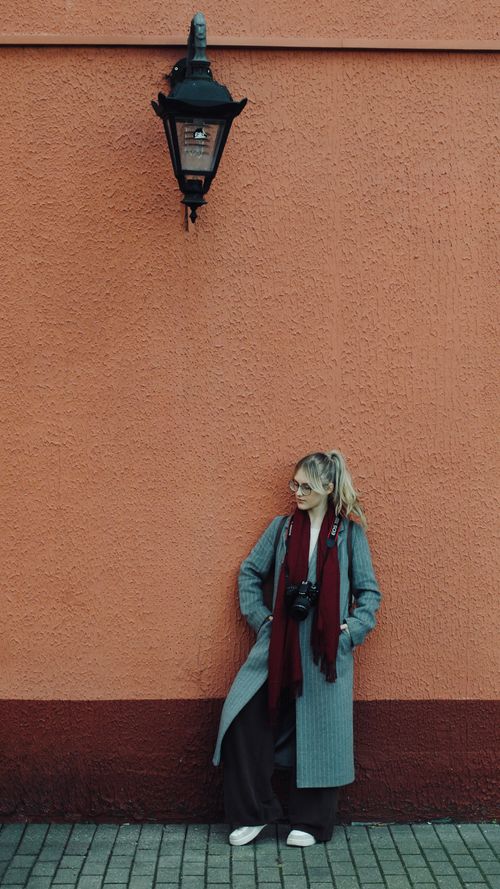 Free A fashionable woman with a camera poses against a vibrant orange wall with a vintage lamp. Stock Photo