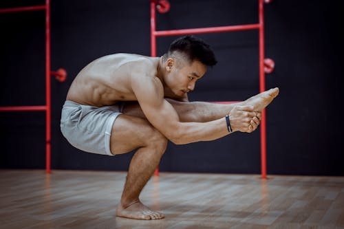 Flexible young Asian man doing balancing asana during Hatha yoga training