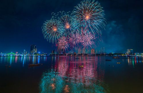 Free Vibrant fireworks illuminate the night sky over a bustling cityscape, reflecting in the water below. Stock Photo
