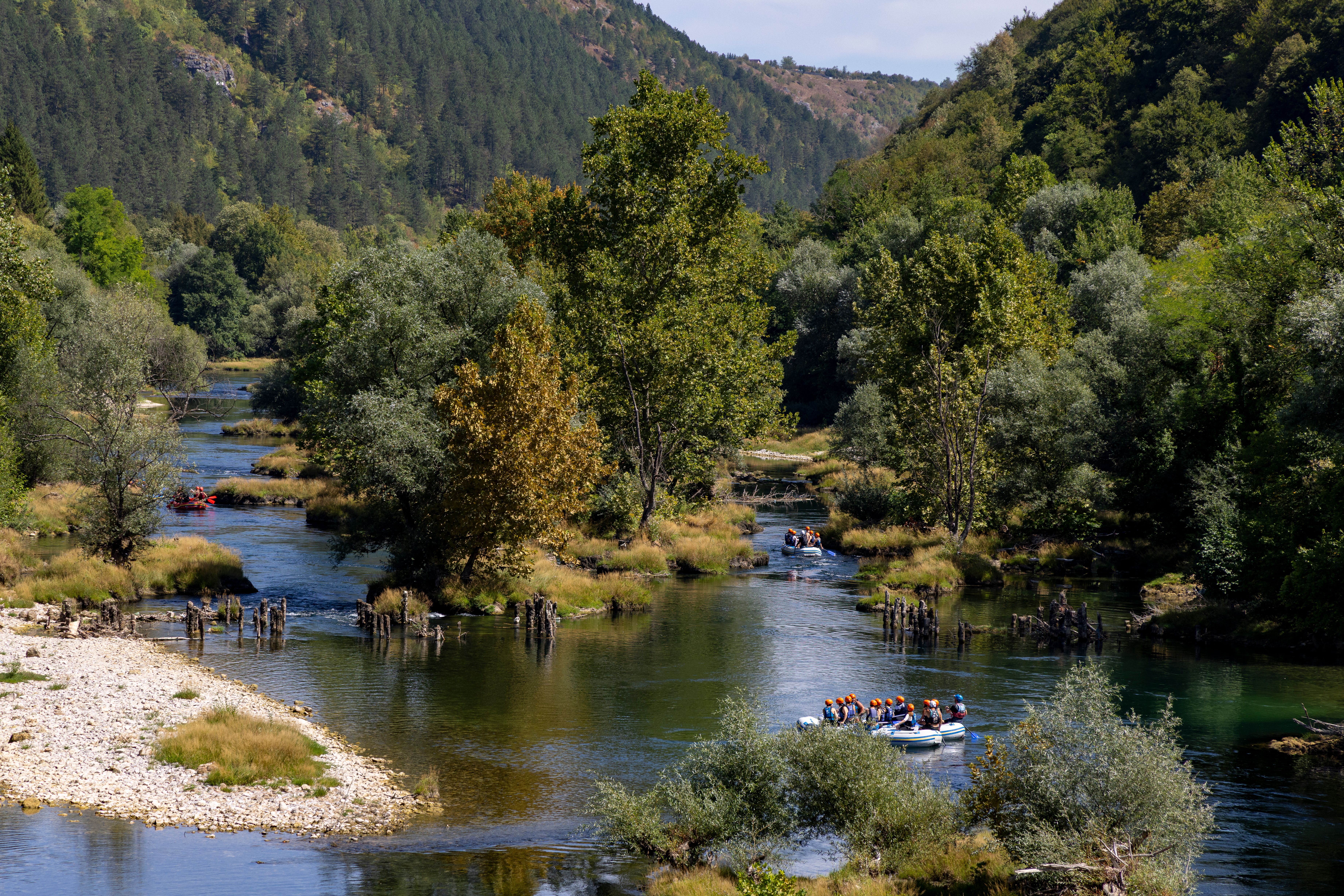 People rafting on the scenic Una River in Bosnia, surrounded by lush green forest.