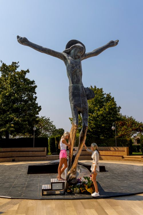 Free Two people admire a modern statue of Jesus outdoors, surrounded by trees. Stock Photo
