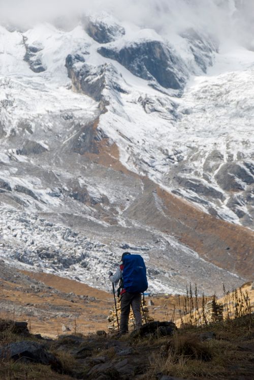 Free A lone hiker with a blue backpack traverses a rugged mountain landscape under a cloudy sky. Stock Photo