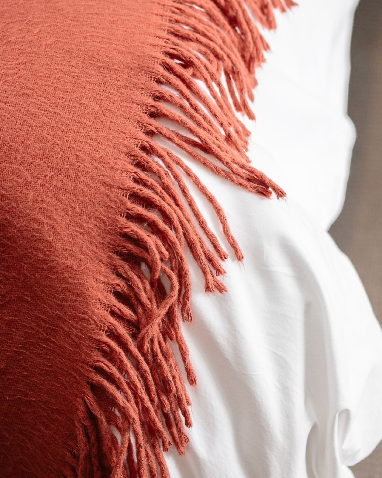 Terracotta fringed wool throw draped over a white bed