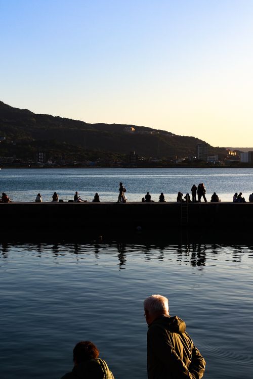 Free People enjoy a peaceful evening stroll on a waterfront promenade with a scenic mountain backdrop. Stock Photo
