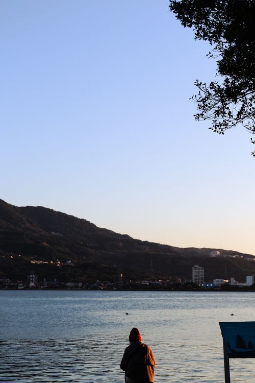 Free A person gazing at a serene lake during sunrise, framed by distant hills. Stock Photo