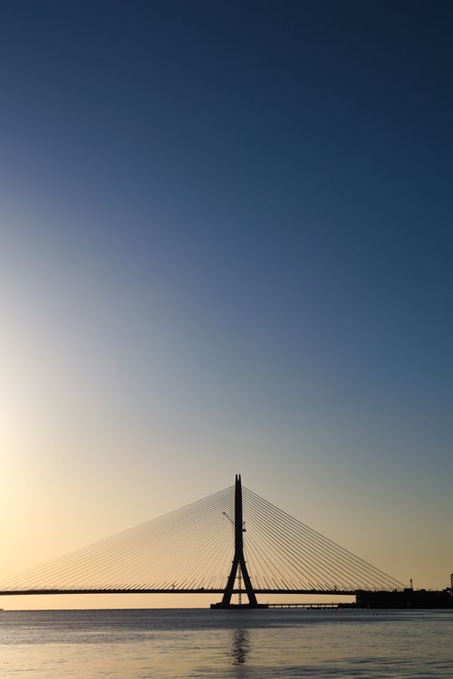 Free Cable-stayed bridge silhouette against a beautiful sunset sky over calm waters. Stock Photo