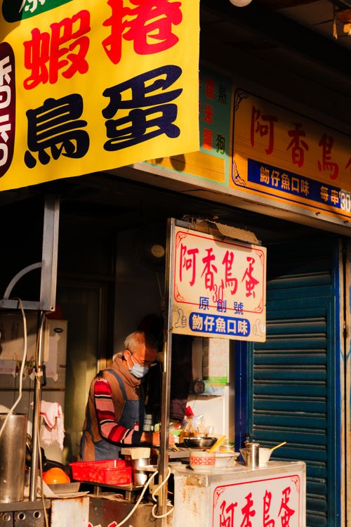 Free Street food vendor preparing dishes at an outdoor market stall with vibrant signage. Stock Photo