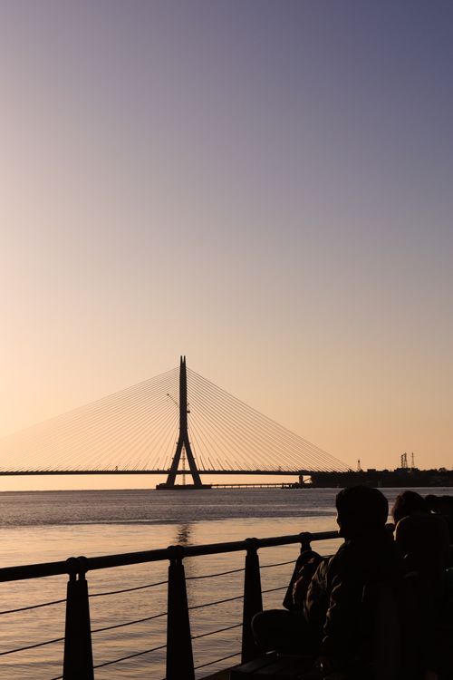 Free A serene sunset view featuring a cable-stayed bridge and silhouettes of people alongside the waterfront. Stock Photo