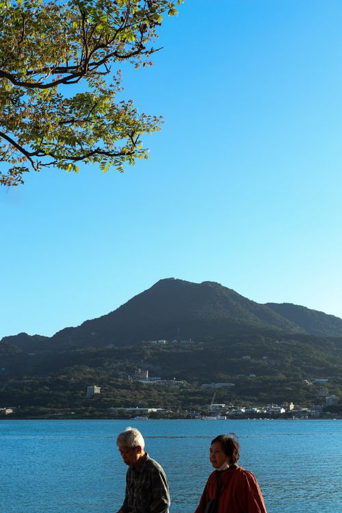 Free Two people walking by a mountain and lake under a blue sky. Stock Photo