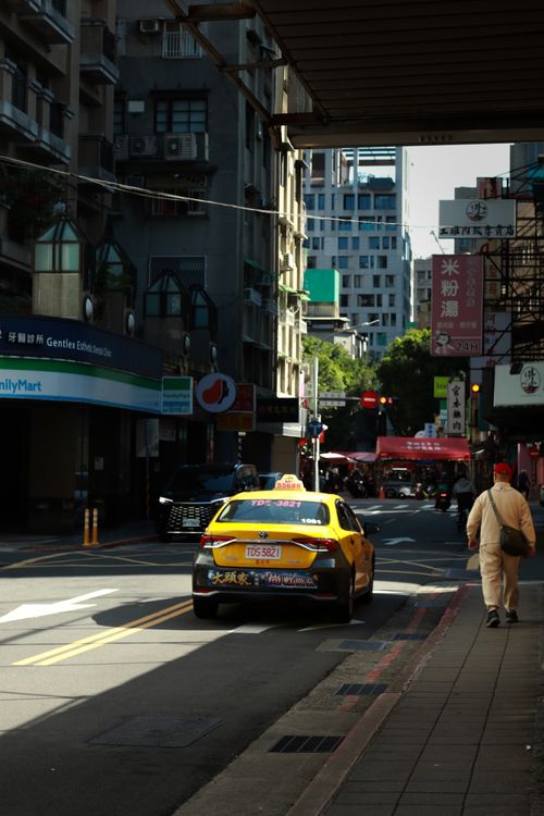 Free A yellow taxi navigates through a lively city street in the daytime, surrounded by urban architecture. Stock Photo