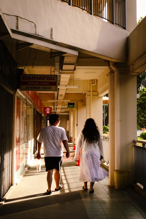 Free A couple strolls through a sunlit corridor in an urban setting, casting long shadows. Stock Photo