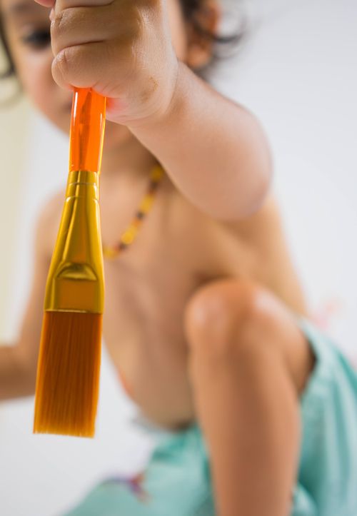 Free A young child artistically holds a bright paintbrush, ready for a creative art project. Stock Photo