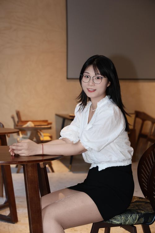 Free Asian woman with glasses smiling, sitting at a table in a café in Hefei, China. Warm indoor setting. Stock Photo