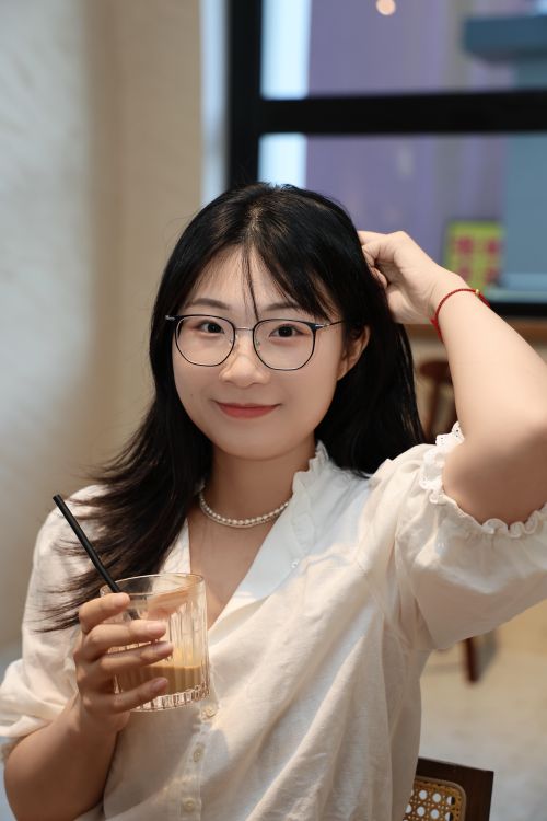 Free Young woman with glasses and a drink, smiling in a cozy indoor setting. Stock Photo