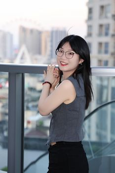 Smiling woman on a Hefei balcony with city skyline in the background. Captured in vibrant daylight.