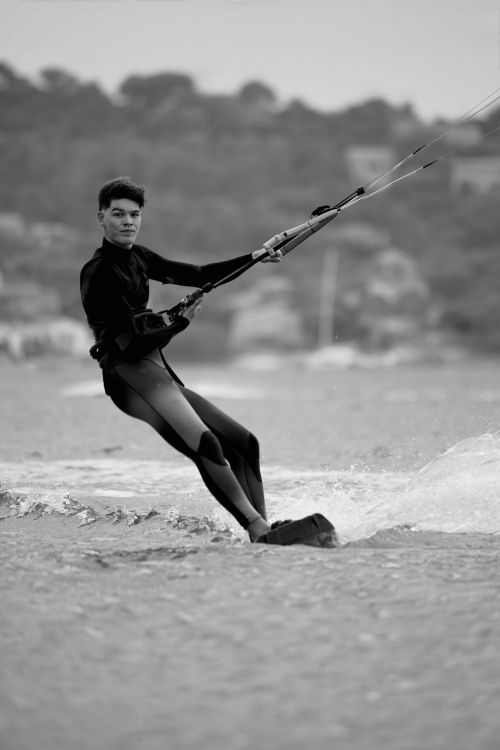 Free Monochrome image of a man kiteboarding against a blurred shoreline backdrop. Stock Photo