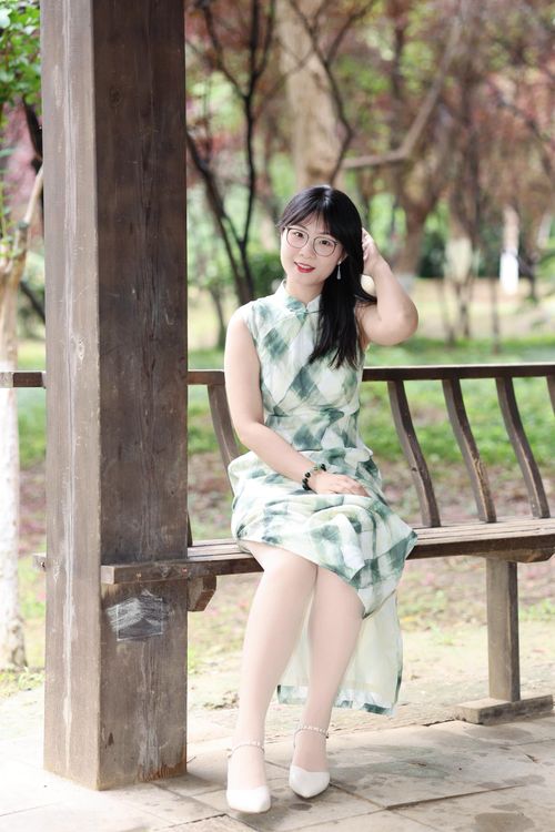Free A woman in a stylish dress smiles while sitting on a park bench in Hefei, China. Stock Photo