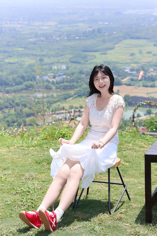 Free A cheerful woman in a white dress enjoys a sunny day sitting on a chair outside. Stock Photo