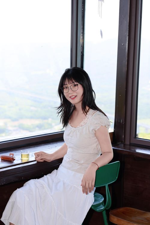 Free Elegant woman in a white dress sitting by a window with a scenic view in Hefei, China. Stock Photo