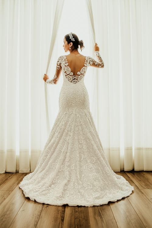 Free Back view full body of anonymous young bride in elegant white dress standing near window and touching curtains before wedding ceremony Stock Photo