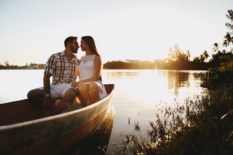 Young Couple Spending Time Together In Wooden Boat Floating On Lake