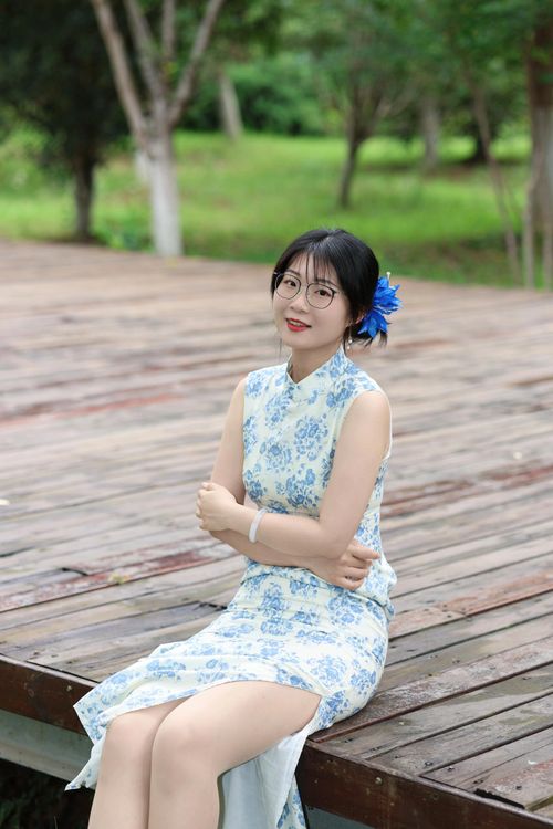 Free A woman in a blue floral cheongsam poses outdoors, exuding elegance and grace. Stock Photo