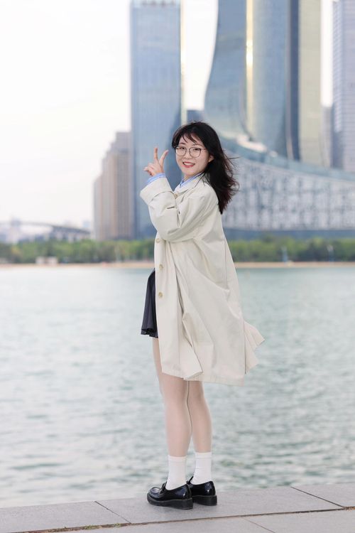 Free A young woman poses stylishly by the lake in Hefei, China, with modern skyscrapers in the background. Stock Photo