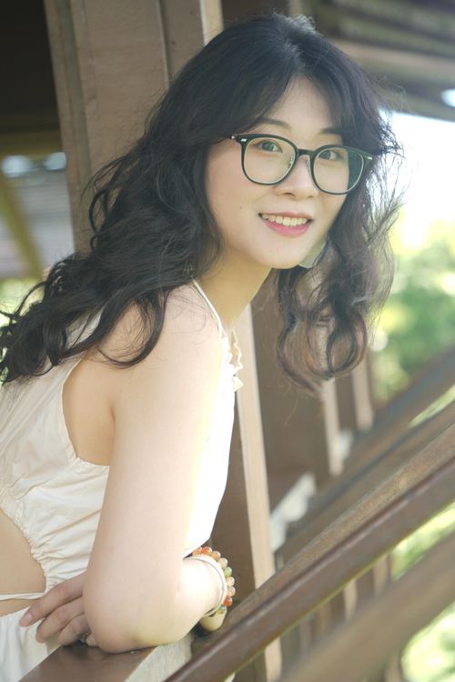 Free Portrait of a young woman with glasses and curly hair smiling while leaning on a balcony. Stock Photo