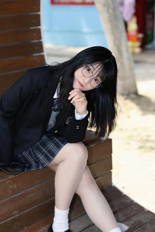Free Teen girl in school uniform sitting outdoors, wearing glasses and a modern outfit, exuding a thoughtful expression. Stock Photo