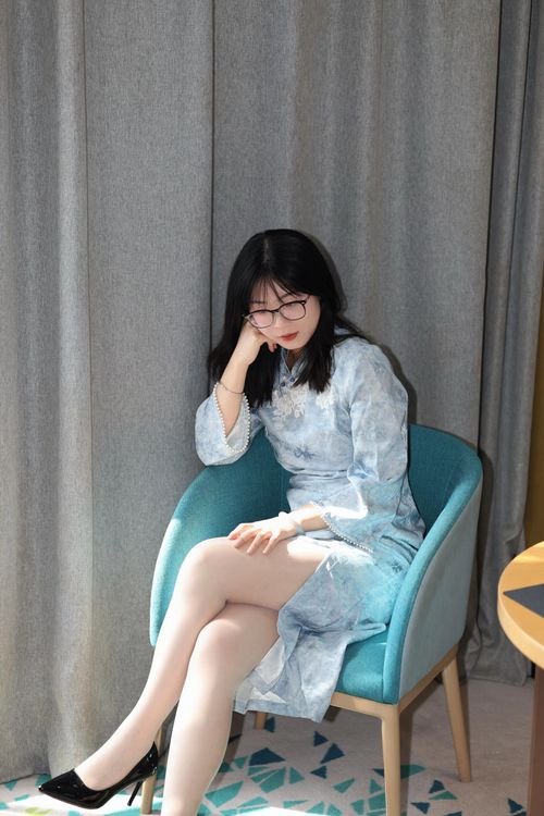 Free A young woman wearing a light blue qipao sits comfortably on a chair indoors. Stock Photo