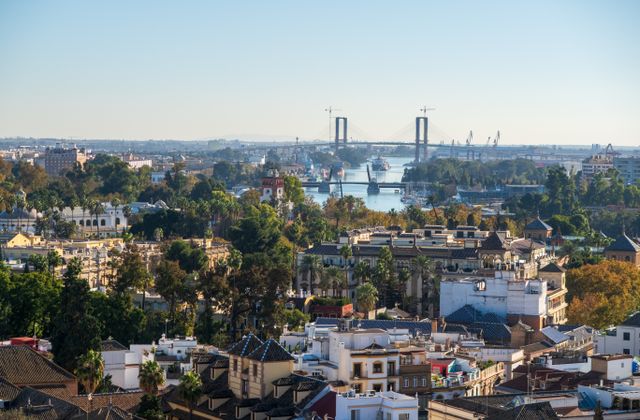 A scenic aerial view of Seville, Spain, showcasing the Isabel II Bridge and cityscape. — arriving in Seville