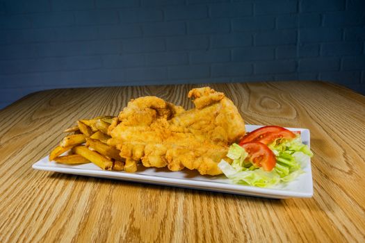 Delicious crispy fried fish served with golden fries and fresh salad on a wooden table.