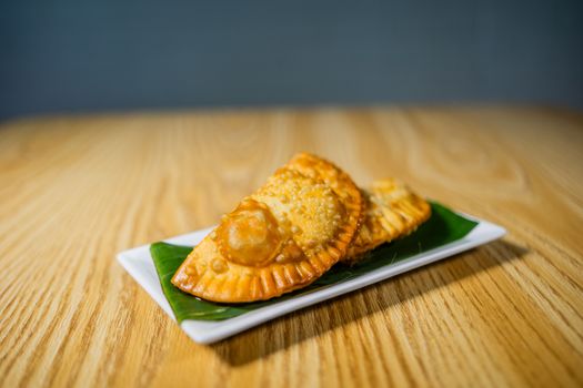 Golden fried empanadas served on a banana leaf lined plate on a wooden table.