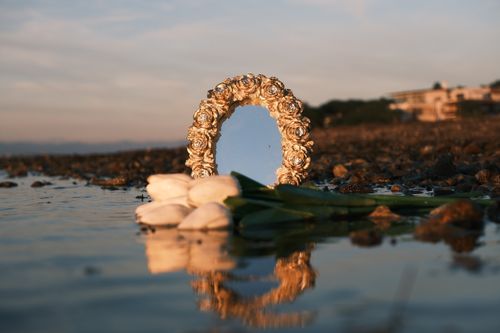 Free A decorative mirror and white flowers reflect beautifully by the coast at sunset. Stock Photo
