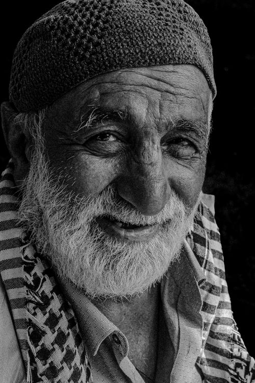 Free Close-up black and white portrait of an elderly man with a warm smile and textured facial features. Stock Photo
