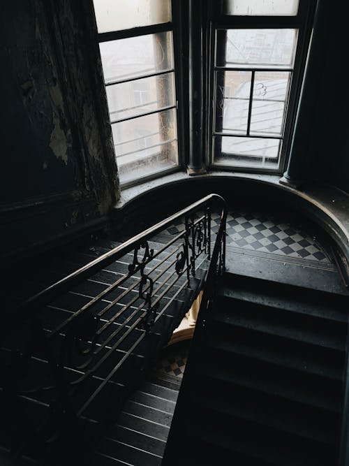 From above of stone stairway and railing in daylight in spacious hall of old building with high ceiling and big narrow windows