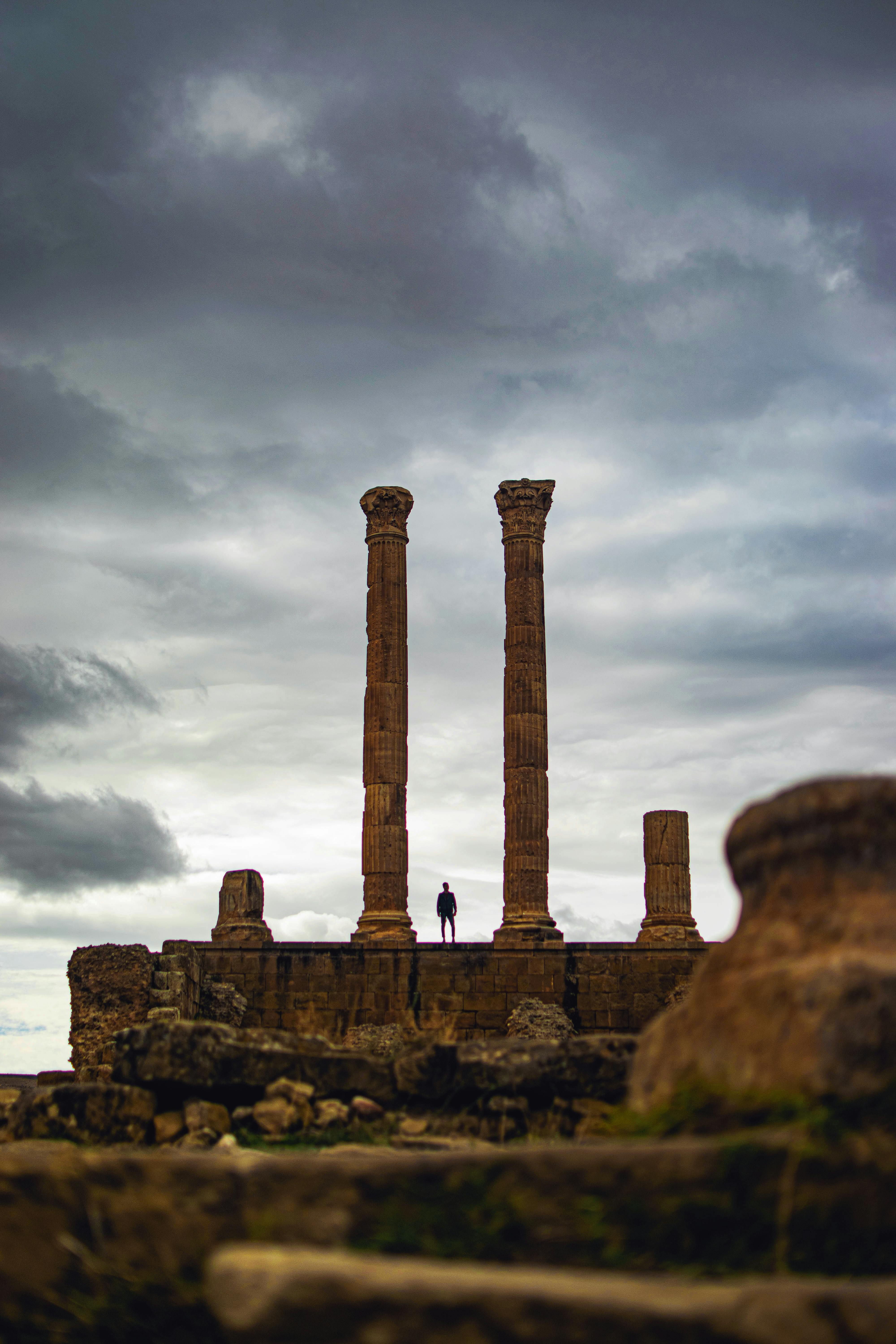 silhouette of person standing in between pillar under cloudy sky