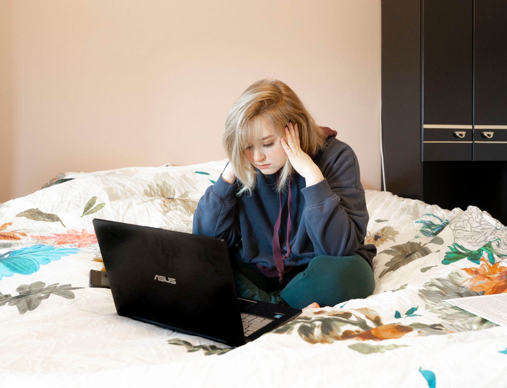 A young person works from bed late at night, the laptop glow standing in for the privacy of a helpline webchat.