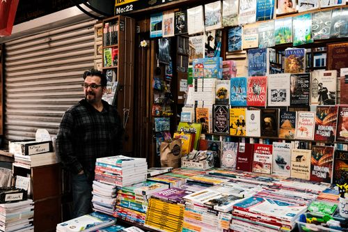 Free A cozy street bookstore with stacks of colorful books and a friendly vendor inside. Stock Photo