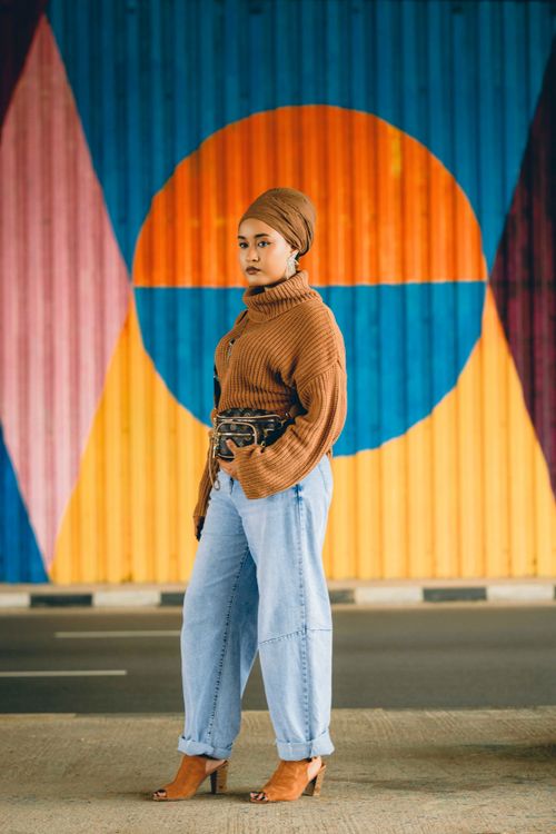 Free Stylish woman in jeans and sweater poses against vibrant Abuja mural. Stock Photo