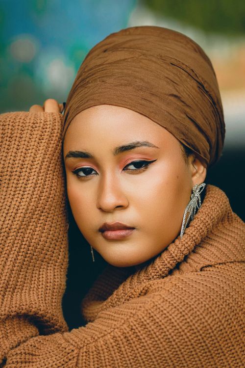 Free Close-up portrait of a woman wearing a brown turban and knitted sweater, looking pensive. Stock Photo